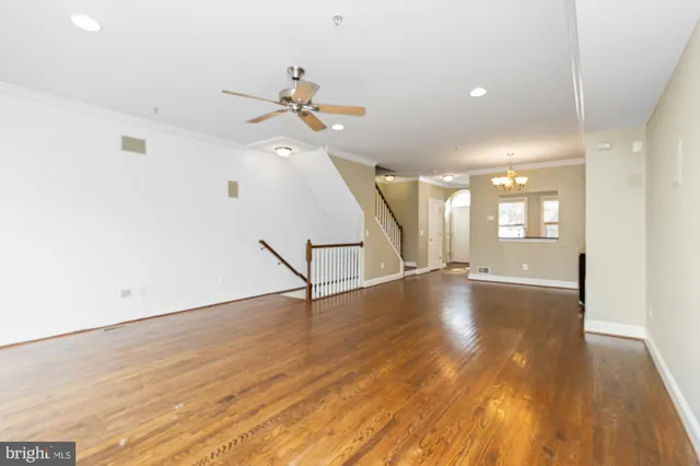 a view of an empty room with wooden floor and a ceiling fan