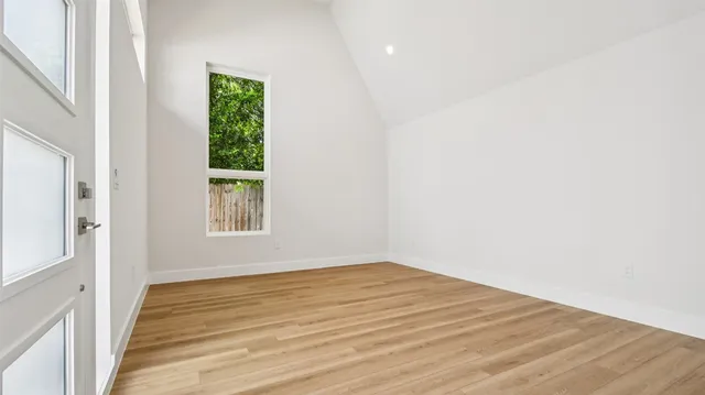 a view of an empty room with wooden floor and a window