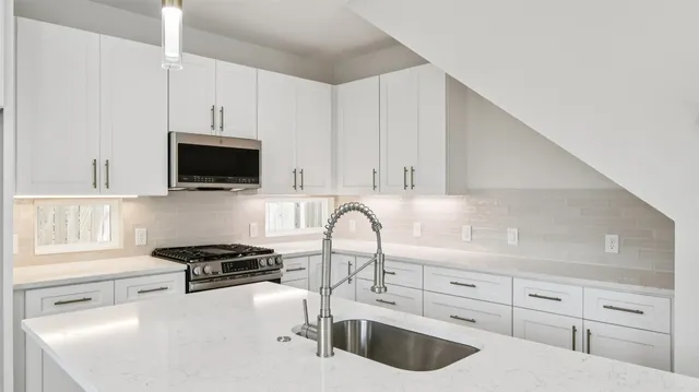 a kitchen with stainless steel appliances granite countertop a sink a stove and a microwave oven with white cabinets