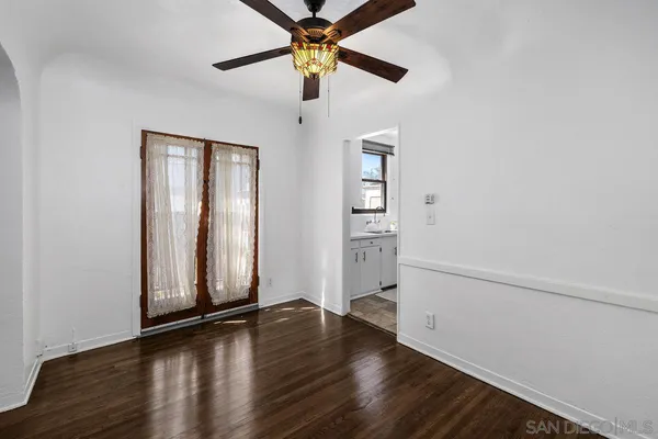 an empty room with wooden floor chandelier fan and windows