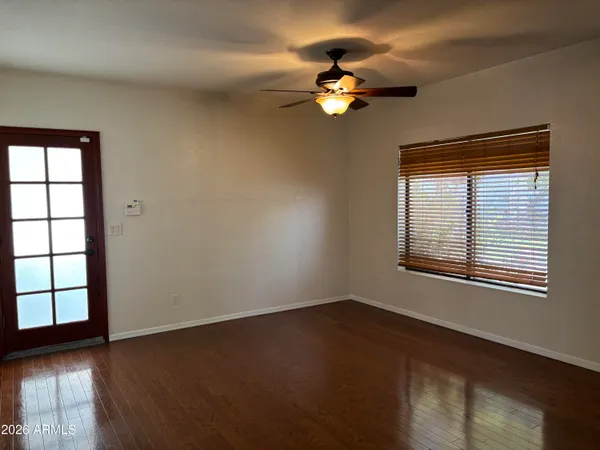 an empty room with wooden floor chandelier fan and kitchen view