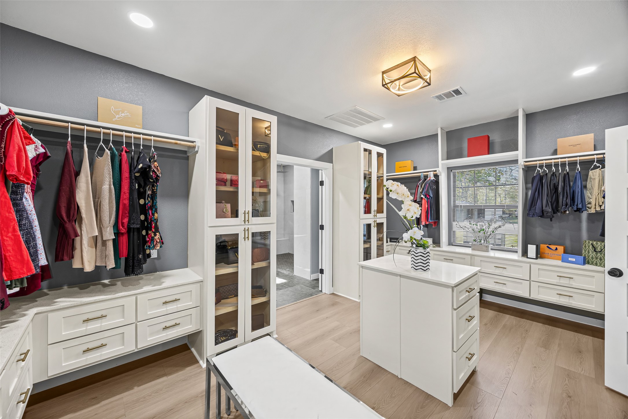 15080 Usher Lane Splendora, TX 77372 - Photo 26 of 44 This photo showcases a spacious, well-organized walk-in closet with ample storage, including drawers, shelves, and hanging space. It features modern lighting, a central island with drawers, and a window for natural light.