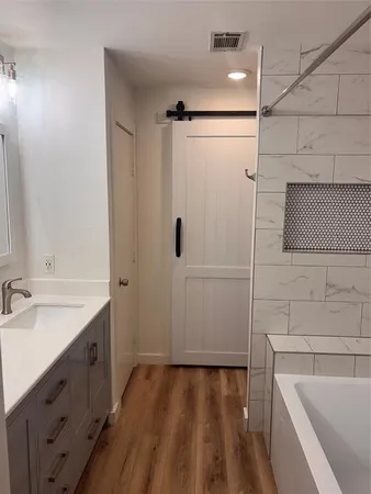 a bathroom with a tub sink vanity granite and shower