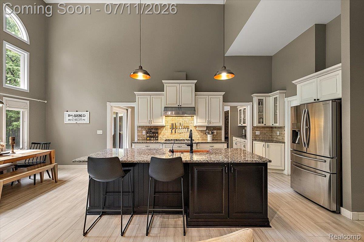 4219 Gardner Road Metamora, MI 48455 - Photo 15 of 87 Spacious kitchen featuring a large central island with seating, stainless steel refrigerator, white cabinetry, tile backsplash, and light wood-finish flooring