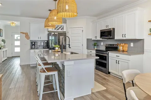 a large white kitchen with kitchen island a refrigerator a sink dishwasher a dining table and chairs with wooden floor