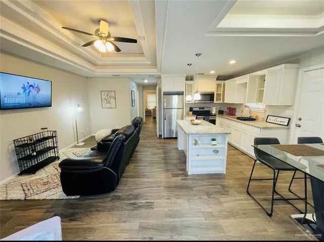 a kitchen with stainless steel appliances kitchen island granite countertop a stove a refrigerator a sink a dining table and chairs with wooden floor