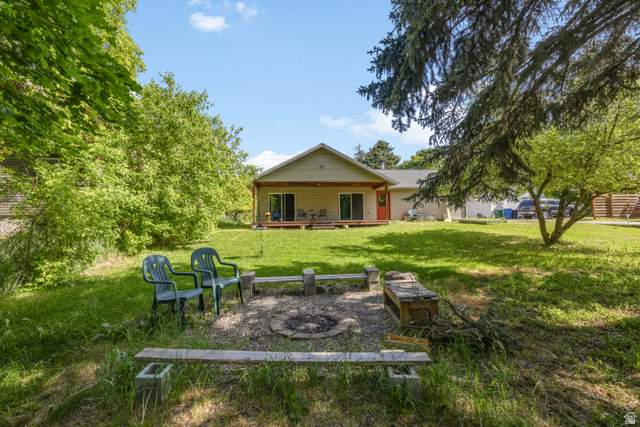 730 East 200 North Logan, UT 84321 - Photo 26 of 28 Spacious yard featuring a built-in fire pit with stone-block seating, expansive lawn, mature trees, and a back deck with sliding glass doors