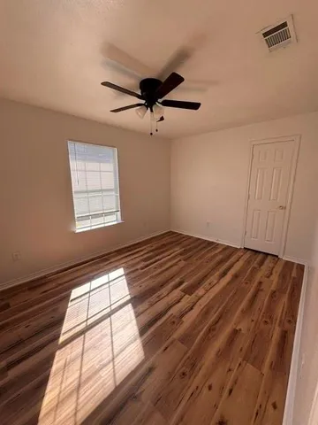a view of empty room with wooden floor and fan