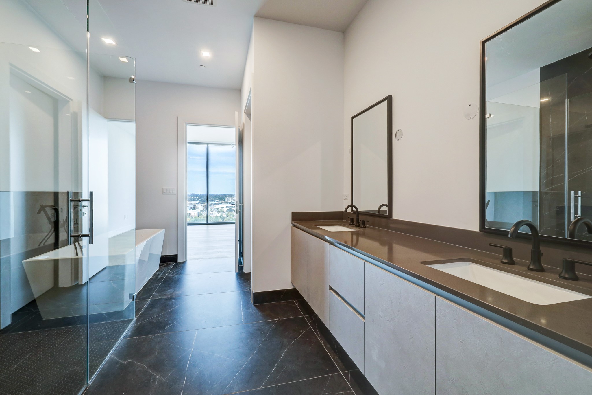 1711 Allen Parkway, Unit 2001 Houston, TX 77019 - Photo 5 of 33 Modern primary bathroom with black porcelain flooring and dual sinks. Features a large glass-enclosed shower, ample counter space, and a door leading to a scenic view, creating a luxurious and functional space.