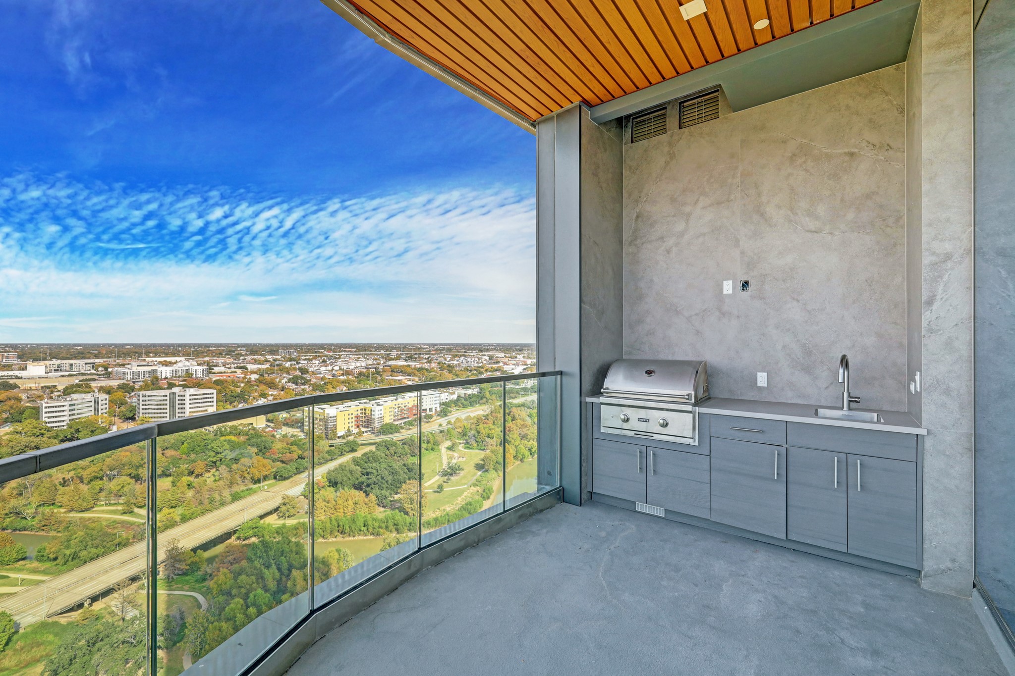 1711 Allen Parkway, Unit 2001 Houston, TX 77019 - Photo 7 of 33 This photo showcases a spacious balcony with a built-in outdoor kitchen, featuring a grill and sink, set against a stunning panoramic view of the cityscape and lush greenery. Perfect for entertaining and enjoying the outdoors.