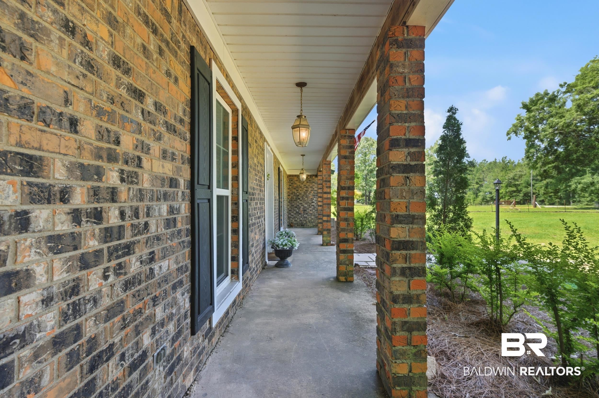 51620 Robert White Road Bay Minette, AL 36507 - Photo 7 of 81 Brick exterior featuring a covered porch with brick columns, concrete flooring, exterior lighting fixtures, and a landscaped perimeter