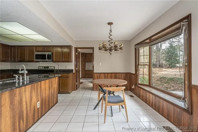 a dining hall with stainless steel appliances granite countertop a stove top oven a sink dishwasher a dining table and chairs with wooden floor