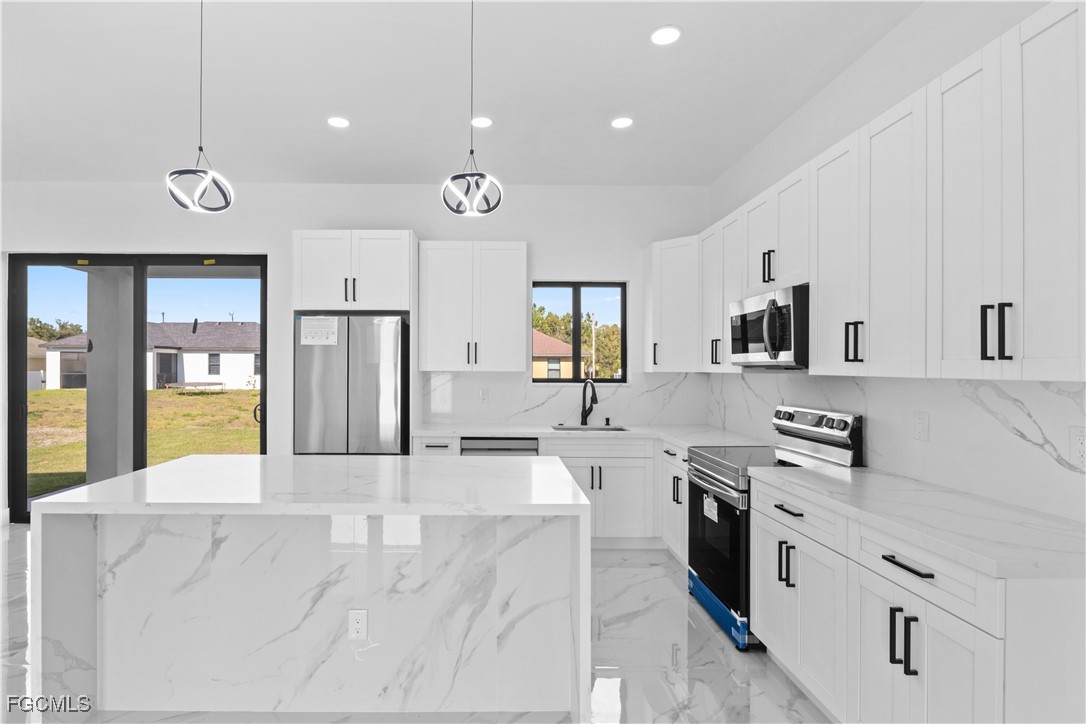 4006 5th Street Southwest Lehigh Acres, FL 33976 - Photo 13 of 32 a large kitchen with stainless steel appliances kitchen island granite countertop a stove a sink a refrigerator and a white cabinets with wooden floor