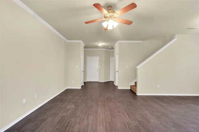 a view of an empty room with wooden floor and a ceiling fan