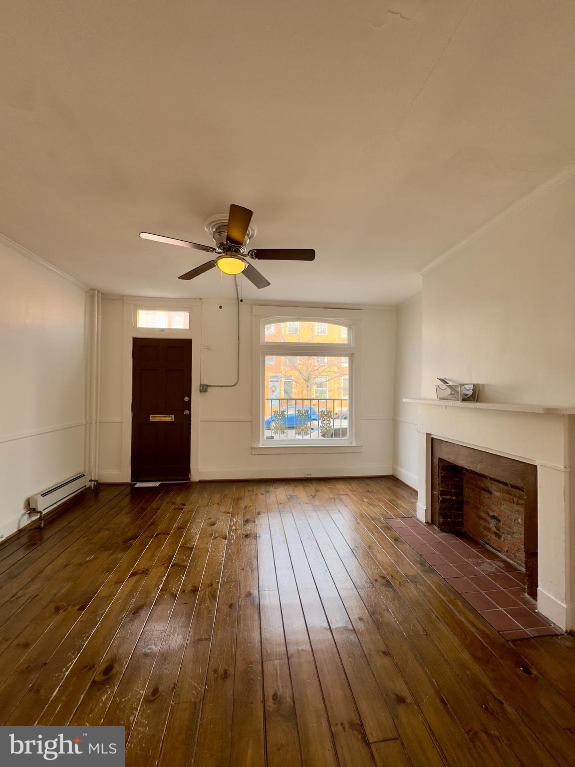 665 Portland Street Baltimore, MD 21230 - Photo 5 of 19 an empty room with wooden floor fireplace and windows