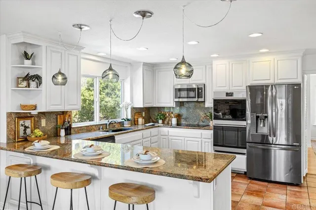a kitchen with stainless steel appliances granite countertop a sink a stove a refrigerator cabinets and a dining table
