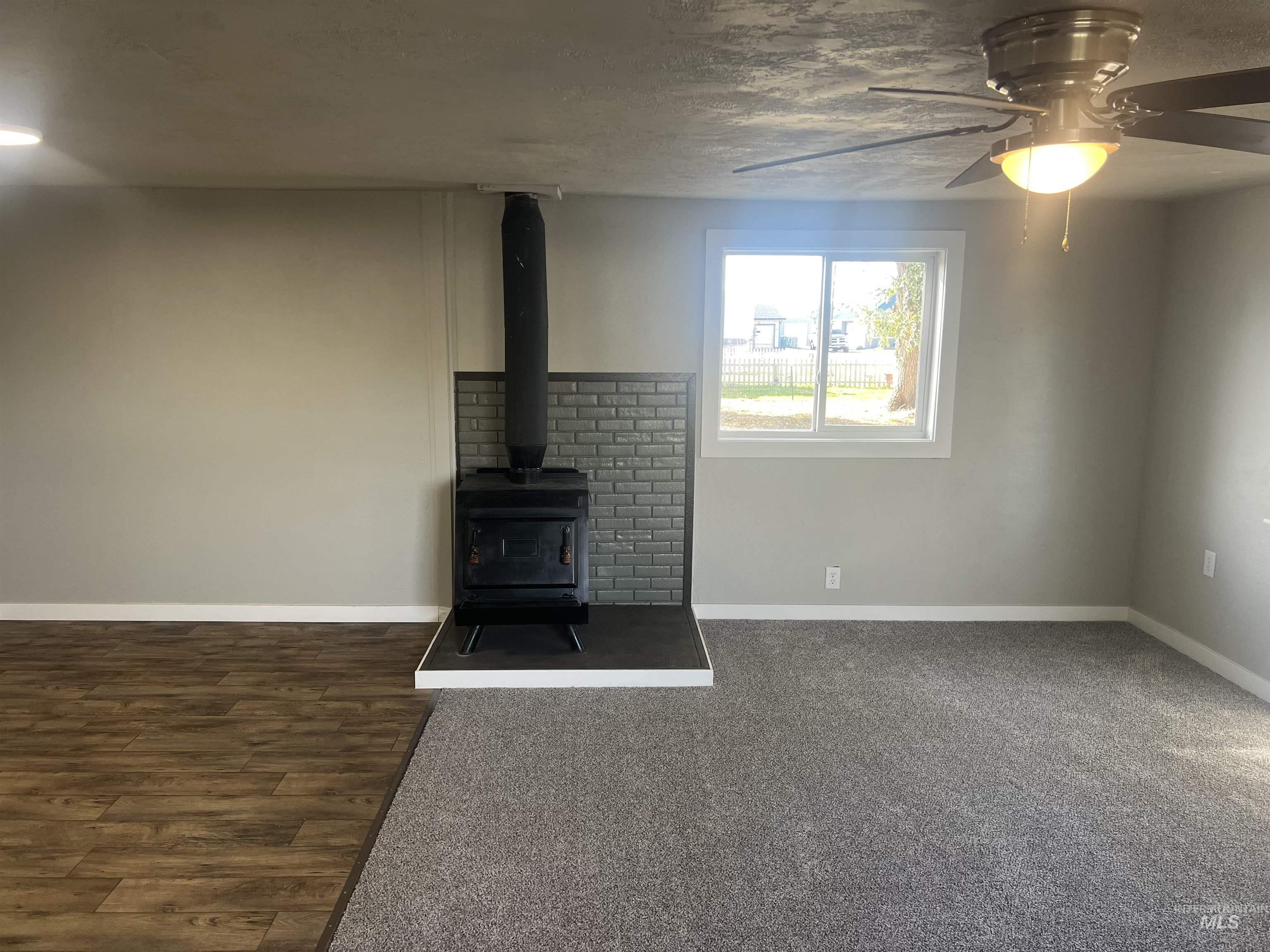 150 Roosevelt Street Mountain Home, ID 83647 - Photo 5 of 16 Unfurnished living room featuring a wood stove, a ceiling fan, and a textured ceiling