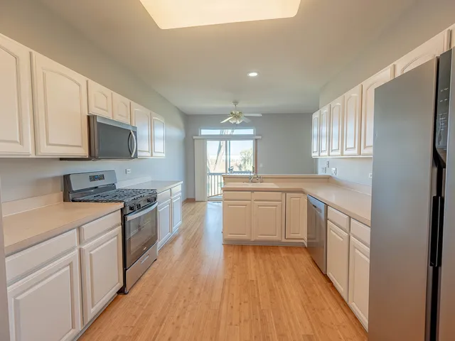 a kitchen with stainless steel appliances a stove top oven a sink a refrigerator white cabinets and wooden floor