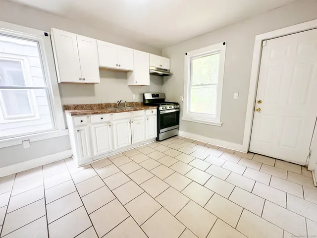 a large white kitchen with granite countertop white cabinets a sink a stove a refrigerator and white cabinets