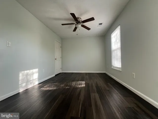an empty room with wooden floor fan and windows