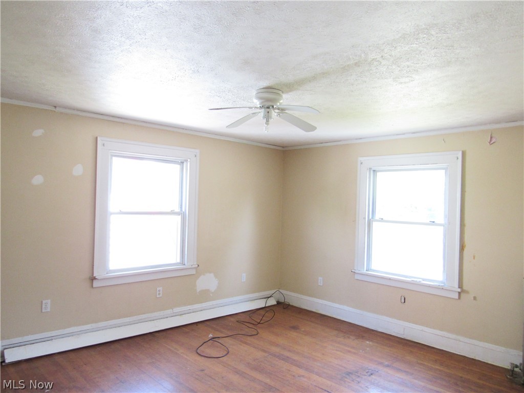 1726 Lee Road Cleveland Heights, OH 44118 - Photo 17 of 36 Room featuring wood-finish flooring, two large windows with white trim, a ceiling fan, and baseboard heating