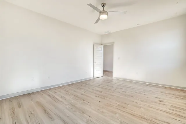 an empty room with wooden floor ceiling fan and windows