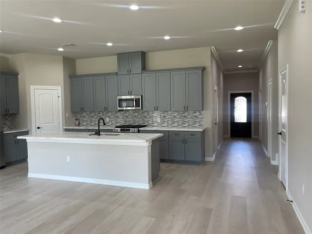 a large kitchen with stainless steel appliances a large counter top a stove a refrigerator cabinets and a wooden floor