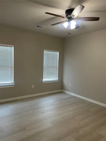 an empty room with wooden floor fan and windows
