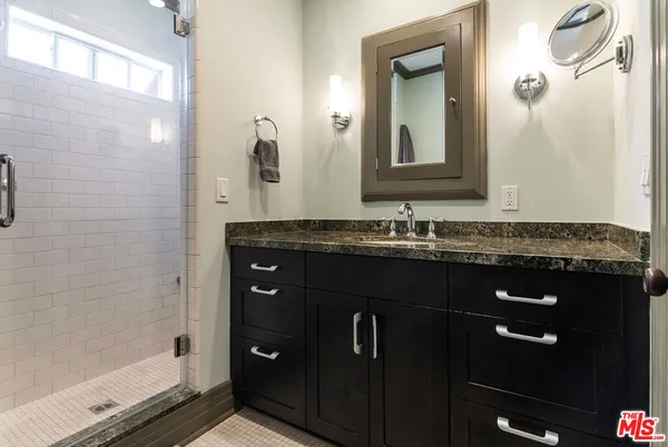 a bathroom with a granite countertop sink a mirror and shower