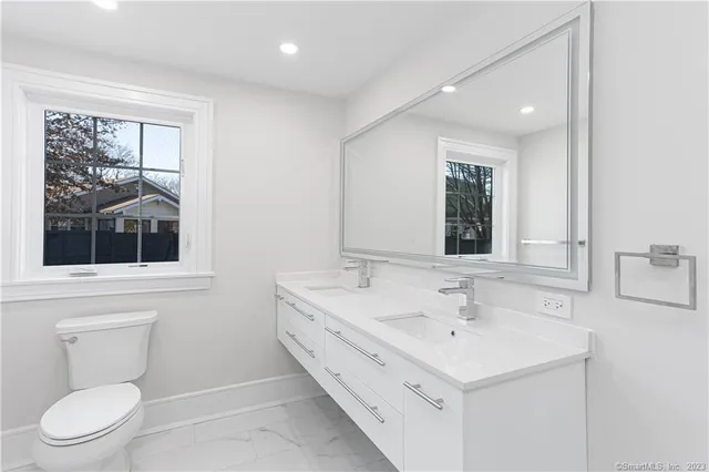 a bathroom with a toilet a sink a mirror and a window