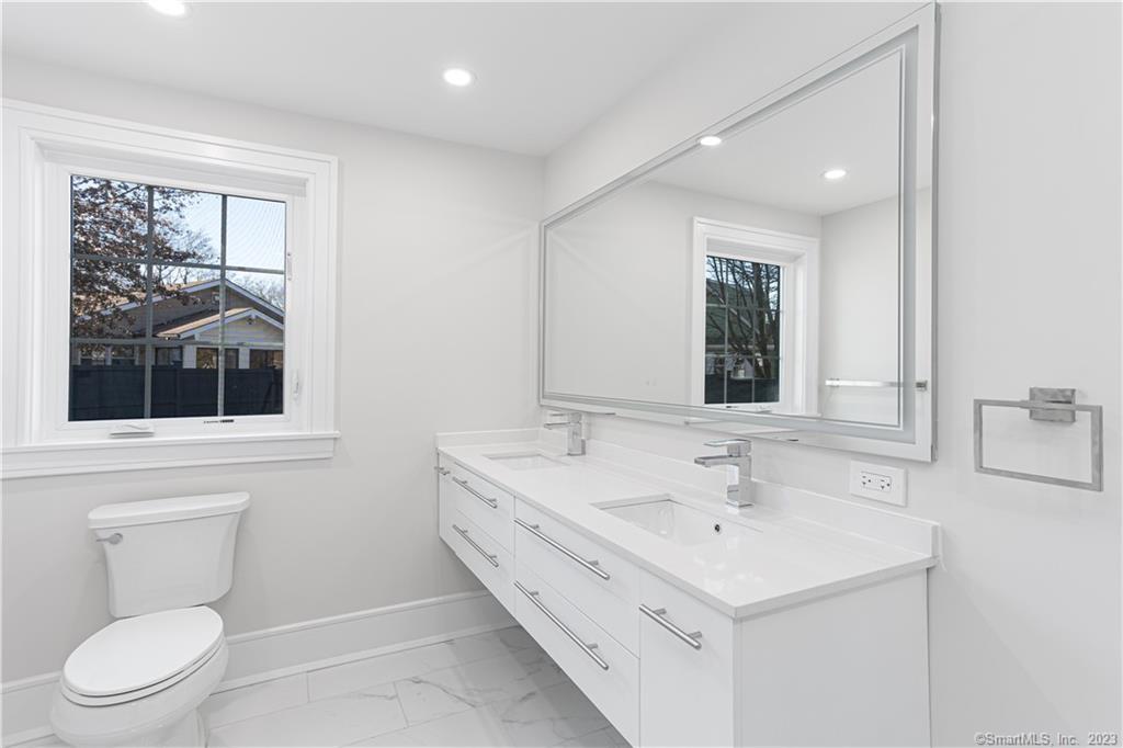 a bathroom with a toilet a sink a mirror and a window