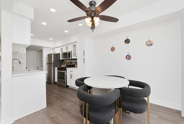 a kitchen with stainless steel appliances kitchen island granite countertop a refrigerator a stove top oven a sink with island chairs and wooden floor