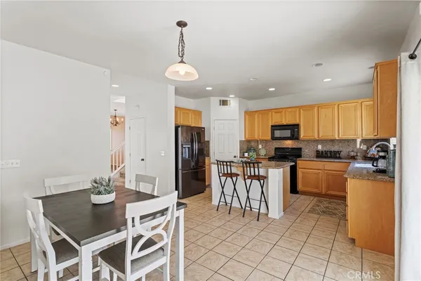 a kitchen with stainless steel appliances kitchen island granite countertop a refrigerator a stove a sink a dining table and chairs with white cabinets