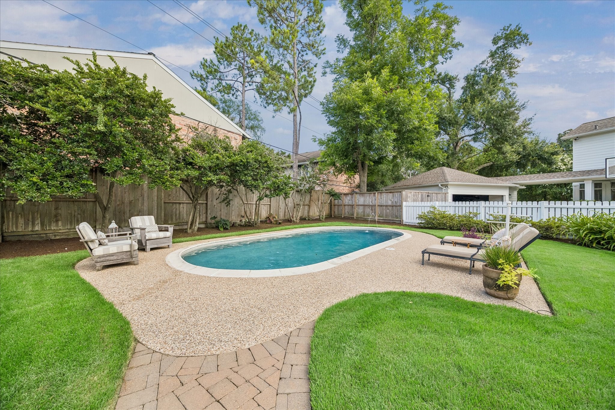12615 Taylorcrest Road Houston, TX 77024 - Photo 27 of 29 This backyard features a serene in-ground pool surrounded by lush greenery and a well-maintained lawn. There are comfortable seating areas, perfect for relaxation or entertaining. The area is enclosed by a wooden fence for added privacy.