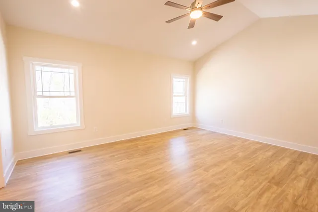 an empty room with wooden floor fan and windows