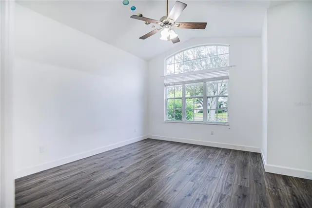 an empty room with wooden floor chandelier fan and windows