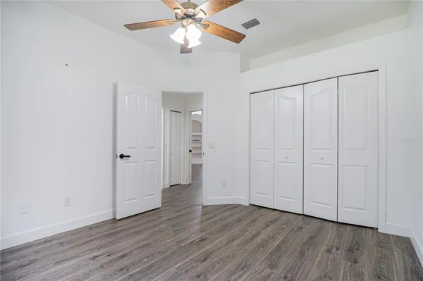 an empty room with wooden floor chandelier fan and closet area