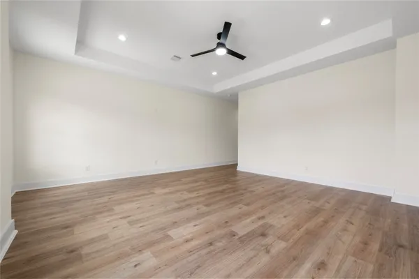 a view of an empty room with wooden floor and a ceiling fan