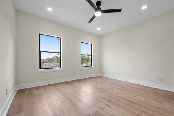 an empty room with wooden floor ceiling fan and windows