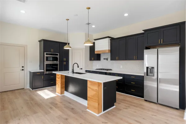 a kitchen with stainless steel appliances granite countertop a refrigerator a sink dishwasher a stove and white countertops with wooden floor