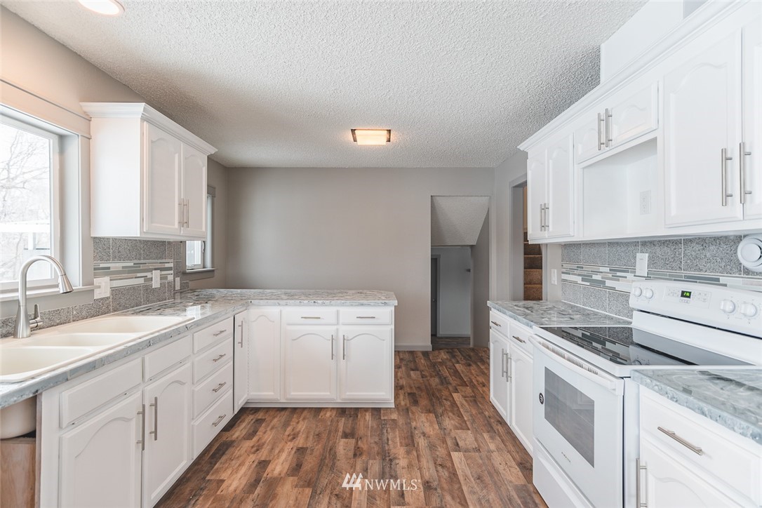 8037 Valley Road Northeast Moses Lake, WA 98837 - Photo 22 of 39 a kitchen with a sink dishwasher stove and white cabinets with wooden floor