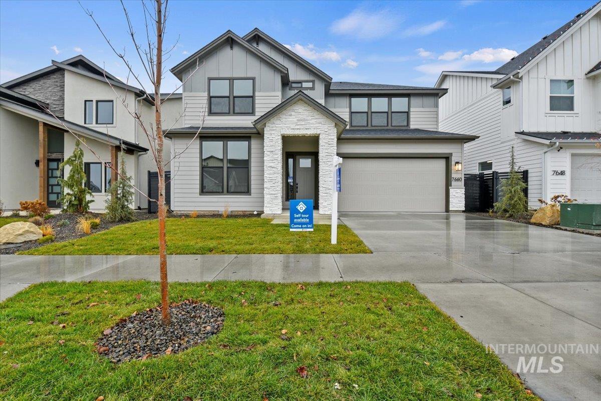 View of front of property with stone siding, a garage, a front yard, concrete driveway, and board and batten siding