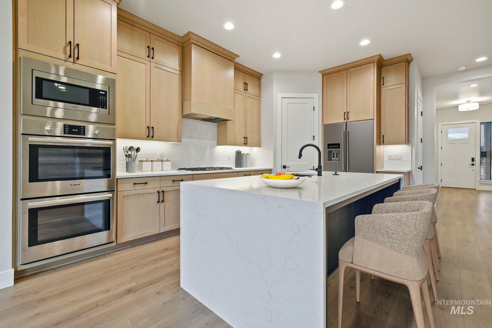 Kitchen featuring light brown cabinetry, appliances with stainless steel finishes, light stone countertops, a breakfast bar, and light wood-type flooring
