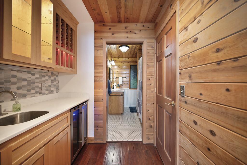 6301 Canyon Creek Road Georgetown, CA 95635 - Photo 24 of 87 bar featuring glass insert cabinets, light brown cabinetry, dark wood-style floors, wood walls, and light stone countertops