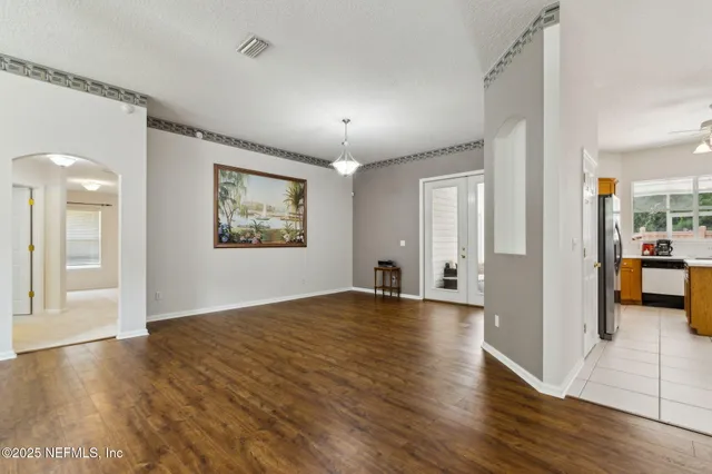 an empty room with wooden floor and a way to kitchen