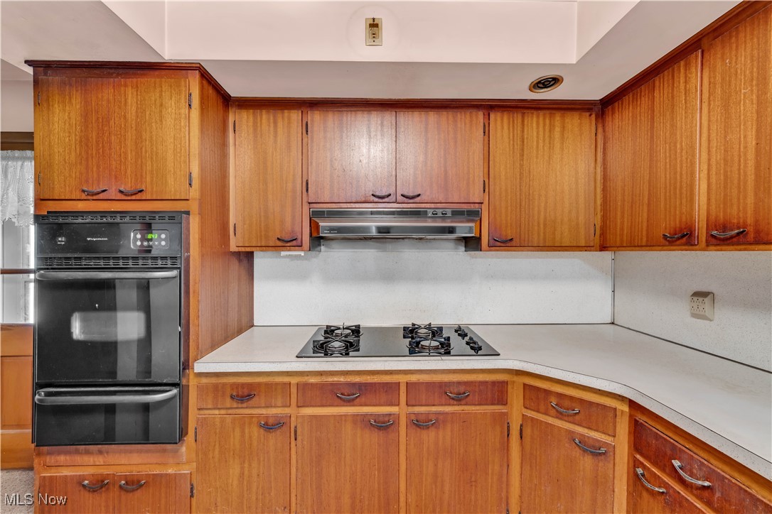 38450 Otten Road North Ridgeville, OH 44039 - Photo 22 of 45 Kitchen featuring black appliances, light countertops, a warming drawer, brown cabinetry, and under cabinet range hood