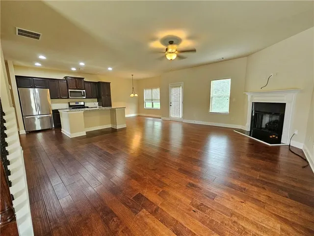 a view of an empty room and kitchen with wooden floor