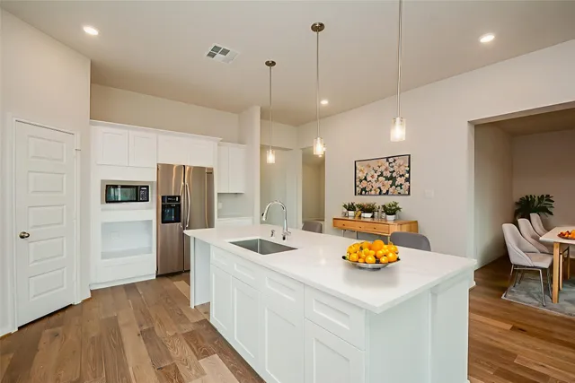 a kitchen that has a dining table wooden floor stainless steel appliances and cabinets