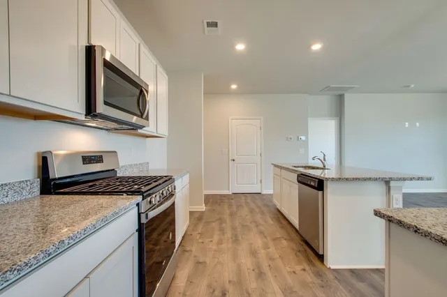 a kitchen with stainless steel appliances granite countertop a stove a sink and a microwave