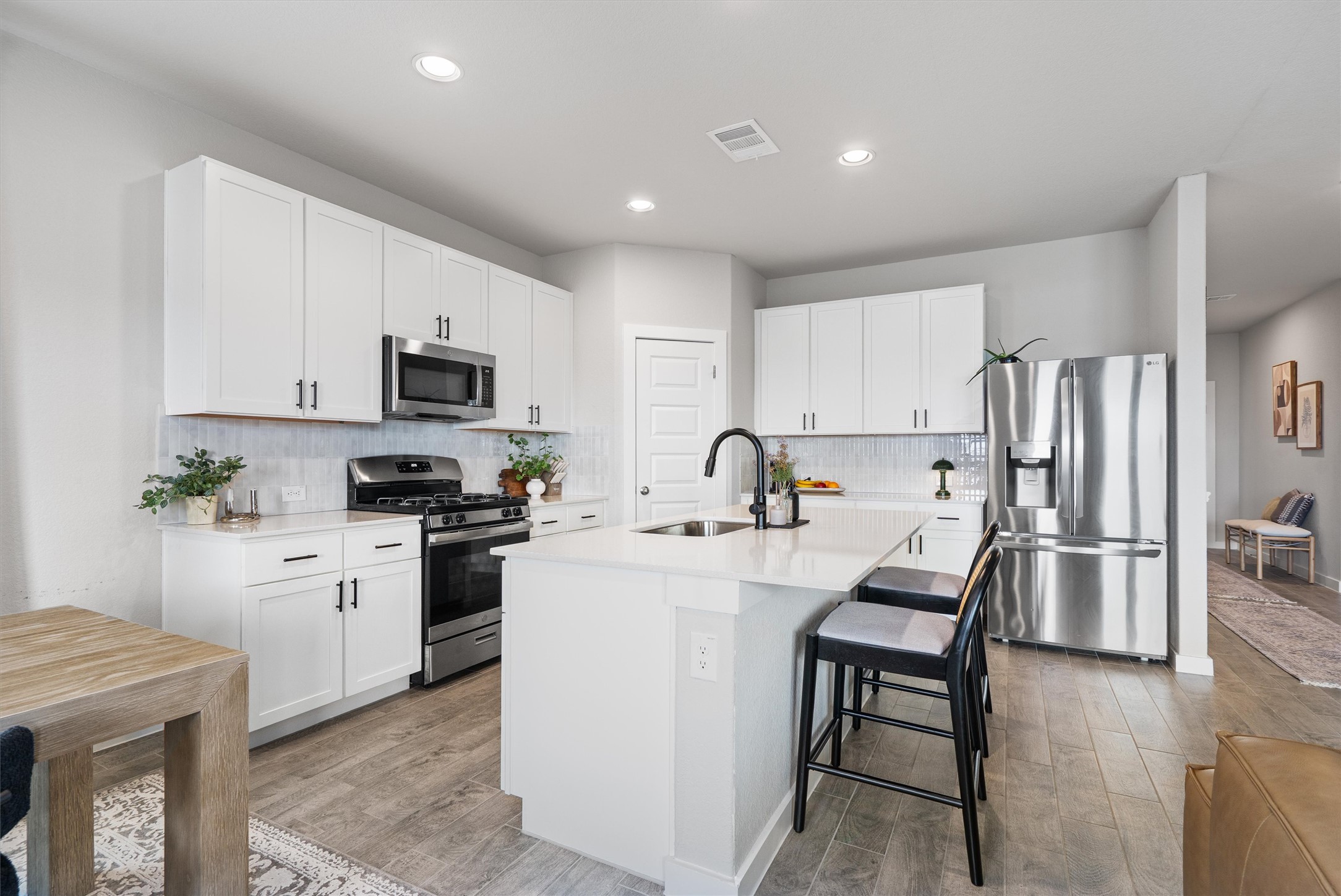 11620 Comano Drive Austin, TX 78747 - Photo 11 of 34 Well-appointed kitchen featuring white cabinetry, stainless steel appliances, a kitchen island with seating, and a large stainless steel refrigerator